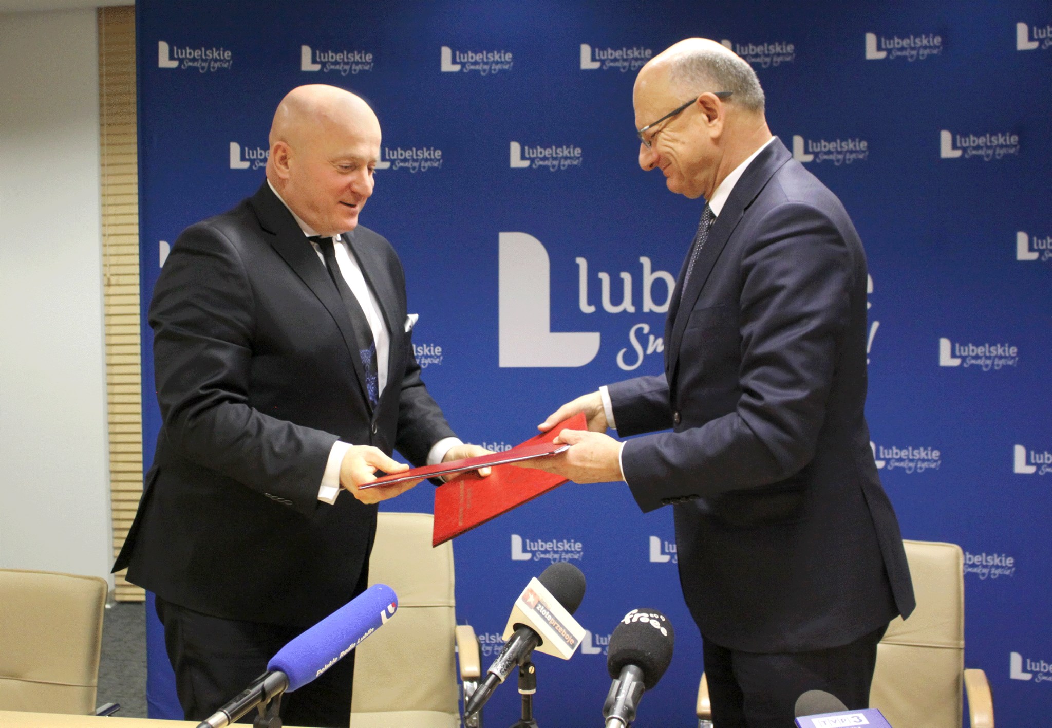 Kolorowa fotografia, sala konferencyjna, na tle flag Unii Europejskiej i Polski marszałek Jarosław Stawiarski wymienia się dokumentami z podpisania umowy z prezydentem Krzysztofem Żukiem